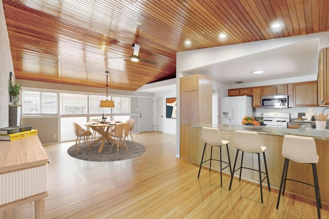 kitchen with lofted ceiling, a breakfast bar area, light wood-style flooring, white appliances, and brown cabinets