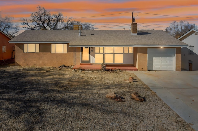 view of front facade featuring driveway, a shingled roof, a chimney, an attached garage, and stucco siding