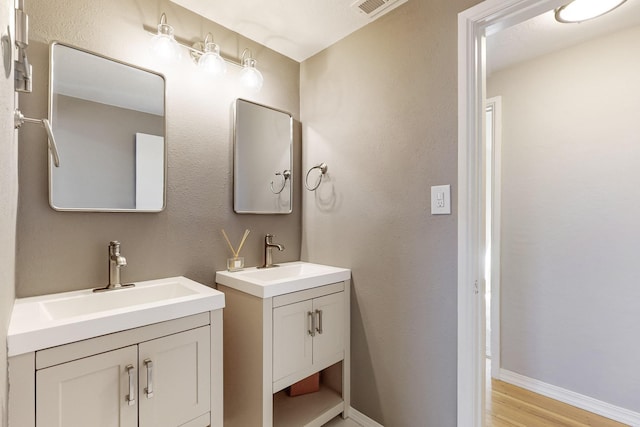 bathroom featuring wood finished floors, two vanities, a sink, and baseboards