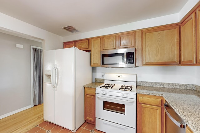 kitchen featuring light stone counters, appliances with stainless steel finishes, brown cabinetry, and visible vents