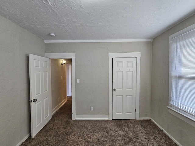 unfurnished bedroom featuring dark colored carpet, a textured ceiling, and multiple windows