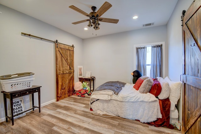 bedroom featuring a barn door, light hardwood / wood-style flooring, and ceiling fan