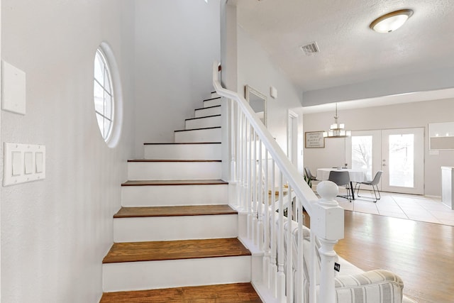 stairway with a textured ceiling, plenty of natural light, french doors, and hardwood / wood-style flooring