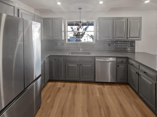 kitchen with tasteful backsplash, stainless steel appliances, sink, a chandelier, and gray cabinets