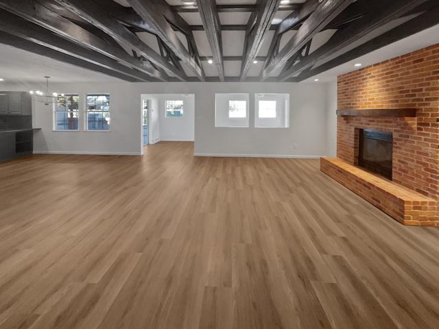 unfurnished living room featuring beam ceiling, light hardwood / wood-style flooring, an inviting chandelier, and a brick fireplace