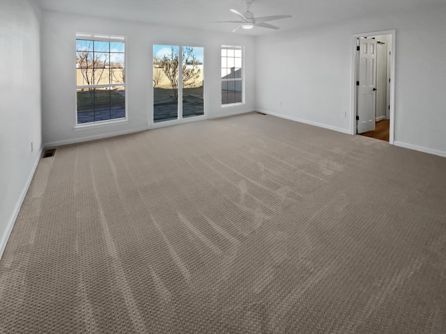 spare room featuring ceiling fan, dark carpet, and a wealth of natural light