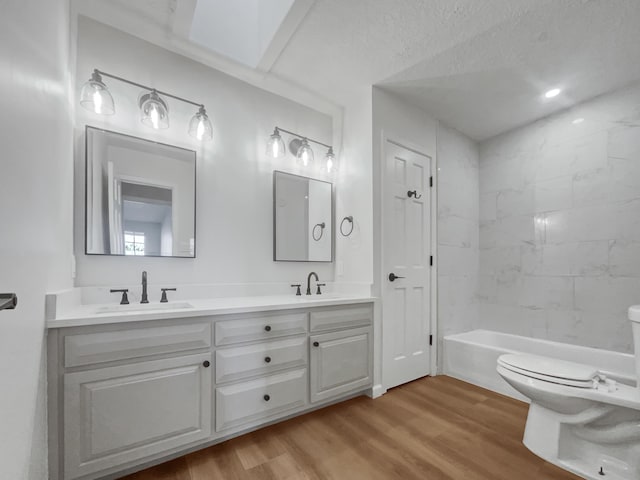 full bathroom featuring wood-type flooring, a textured ceiling, toilet, vanity, and tiled shower / bath