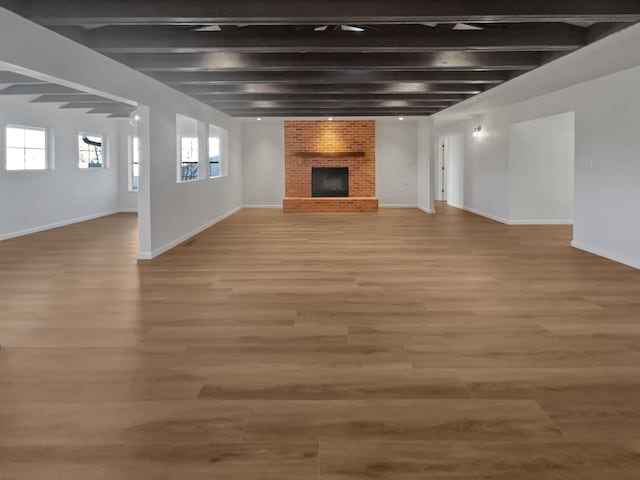 unfurnished living room with beam ceiling, hardwood / wood-style flooring, and a brick fireplace