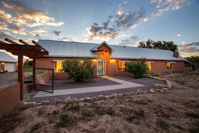 back of house at dusk with metal roof and a pergola