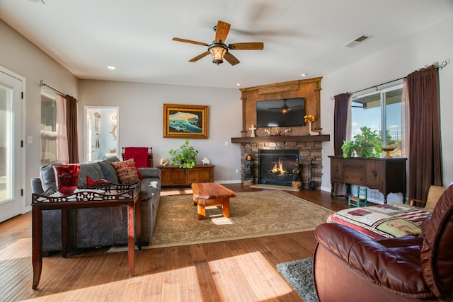 living room with light hardwood / wood-style floors, a stone fireplace, and ceiling fan