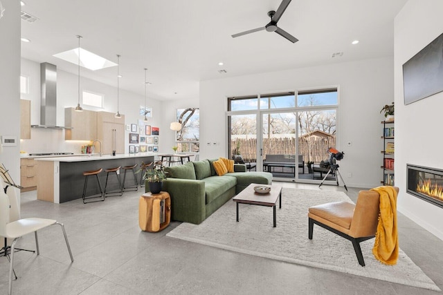 living room with a high ceiling, a skylight, and ceiling fan