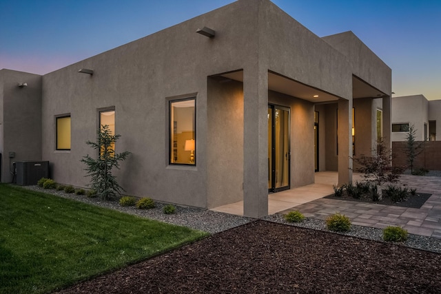 property exterior at dusk with central AC unit, a patio area, and a lawn