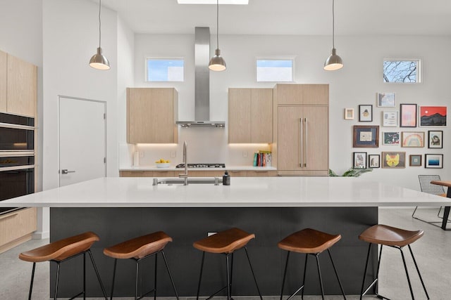 kitchen featuring wall chimney exhaust hood, light brown cabinets, and a large island with sink