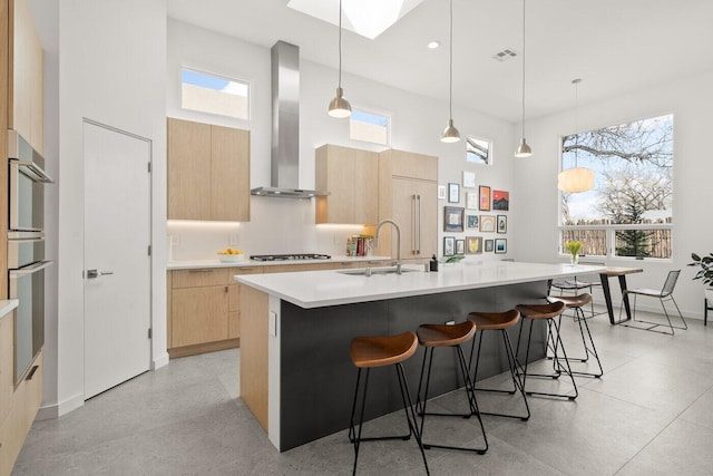 kitchen featuring pendant lighting, a kitchen island with sink, wall chimney exhaust hood, and sink