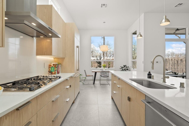 kitchen featuring light brown cabinetry, appliances with stainless steel finishes, sink, wall chimney range hood, and pendant lighting