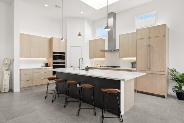 kitchen featuring light brown cabinets, sink, hanging light fixtures, an island with sink, and paneled built in fridge