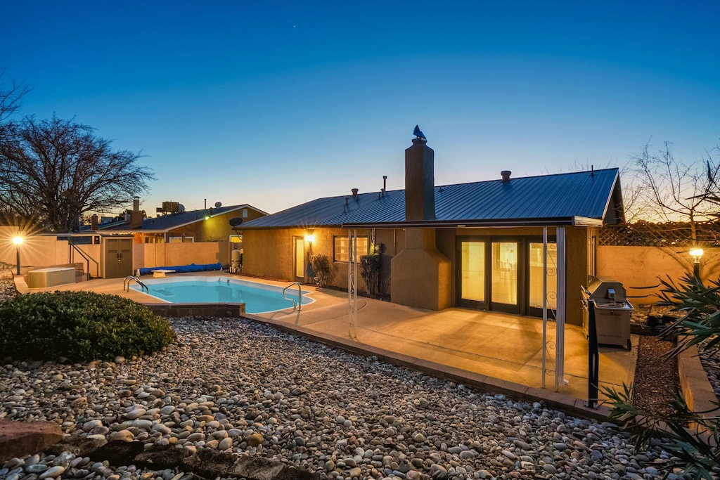 back house at dusk featuring a fenced in pool and a patio area