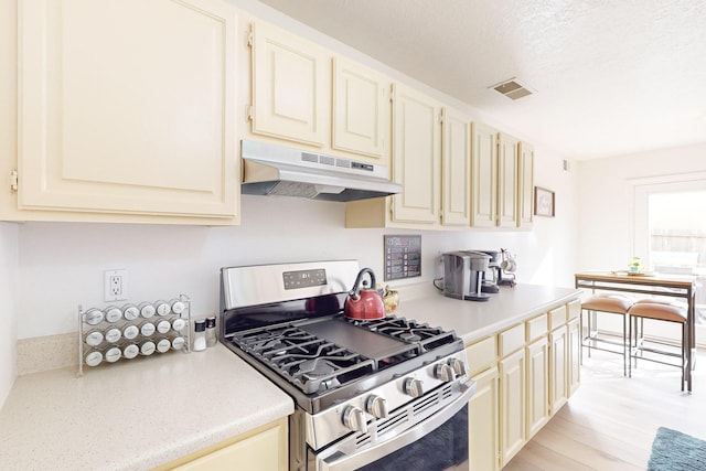 kitchen featuring cream cabinetry, light wood-type flooring, a textured ceiling, and stainless steel range with gas cooktop