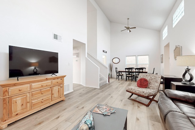 living room featuring ceiling fan, light wood-type flooring, and a high ceiling