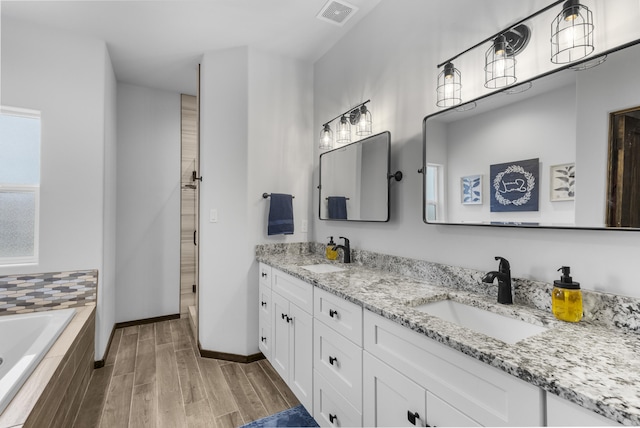 full bath featuring a relaxing tiled tub, visible vents, a sink, and wood finished floors