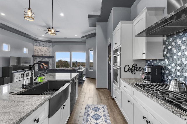 kitchen with a stone fireplace, black gas stovetop, wood finished floors, wall chimney range hood, and decorative backsplash