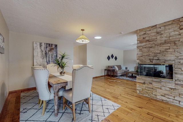 dining area with a textured ceiling, light wood-type flooring, and a stone fireplace