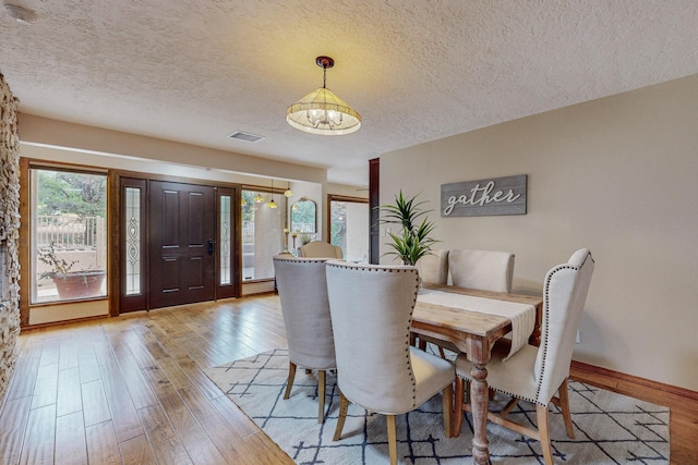 dining area featuring light hardwood / wood-style floors, a textured ceiling, and an inviting chandelier