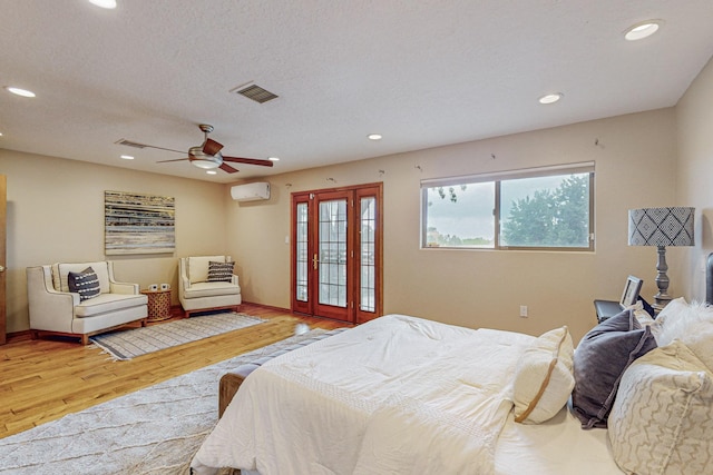 bedroom featuring a textured ceiling, ceiling fan, wood-type flooring, and a wall mounted air conditioner