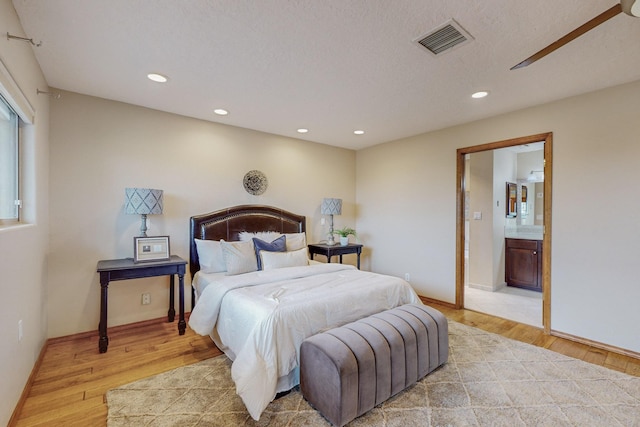 bedroom featuring connected bathroom, light hardwood / wood-style flooring, and a textured ceiling