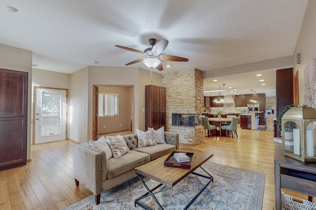 living room featuring ceiling fan, a fireplace, light wood-type flooring, and a textured ceiling