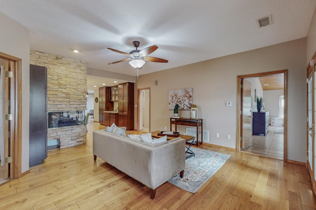 living room featuring a fireplace, light wood-type flooring, and ceiling fan