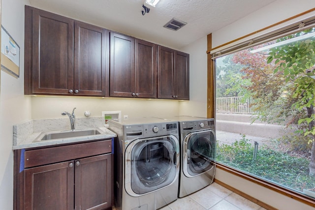 laundry room featuring cabinets, sink, a textured ceiling, light tile patterned flooring, and washing machine and clothes dryer