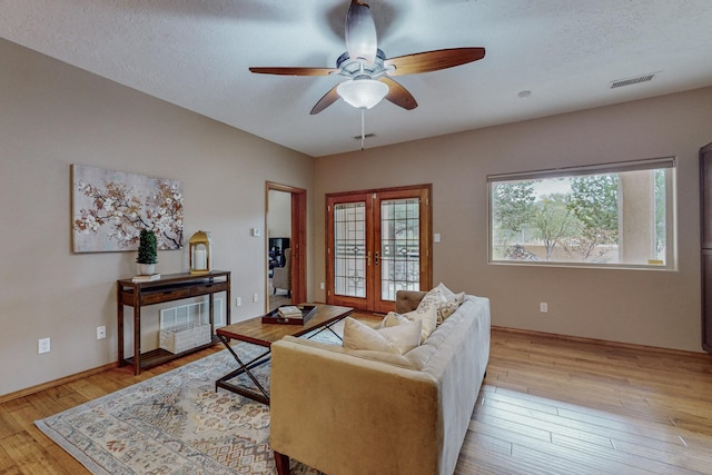 living room with ceiling fan, french doors, a textured ceiling, and light hardwood / wood-style flooring