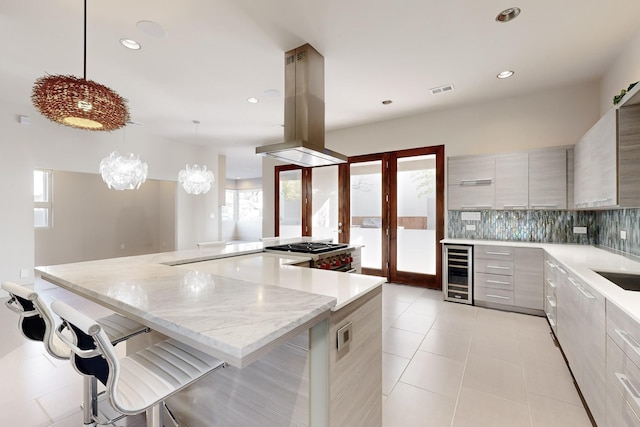 kitchen with tasteful backsplash, wine cooler, a kitchen breakfast bar, decorative light fixtures, and island range hood