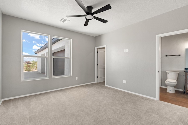 unfurnished bedroom with ceiling fan, light colored carpet, a textured ceiling, and ensuite bath