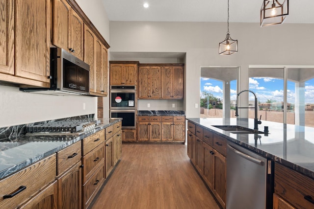 kitchen with dark stone counters, stainless steel appliances, sink, hardwood / wood-style floors, and hanging light fixtures