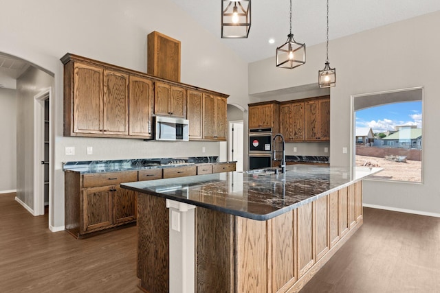 kitchen featuring hanging light fixtures, stainless steel appliances, dark wood-type flooring, dark stone countertops, and a spacious island