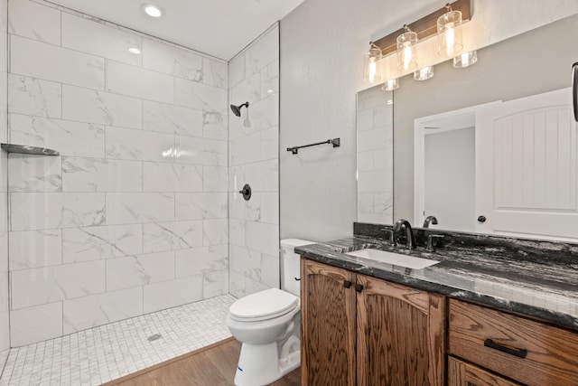 bathroom featuring a tile shower, vanity, hardwood / wood-style flooring, and toilet