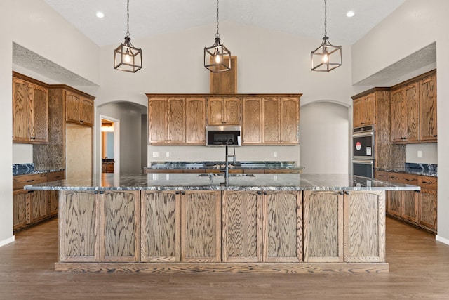 kitchen with a center island with sink, high vaulted ceiling, hanging light fixtures, and appliances with stainless steel finishes