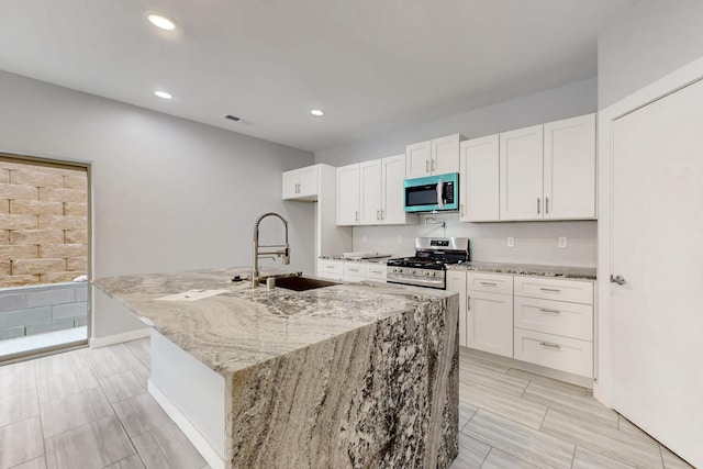 kitchen with white cabinetry, an island with sink, sink, light stone counters, and gas range