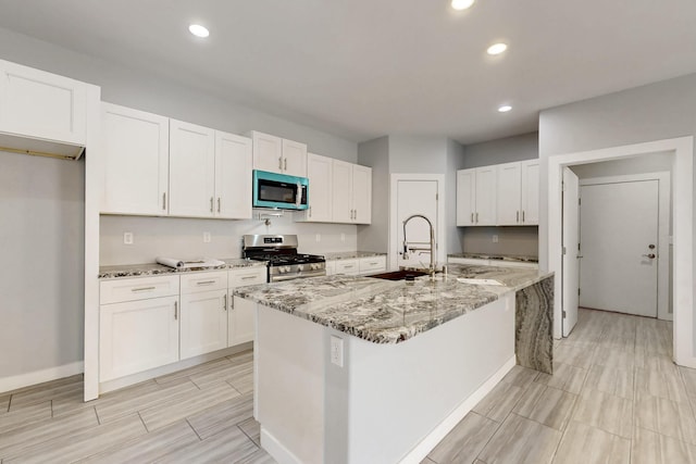 kitchen with light stone counters, gas range, a kitchen island with sink, and white cabinetry