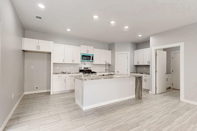 kitchen with sink, appliances with stainless steel finishes, white cabinetry, light stone countertops, and an island with sink