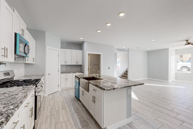 kitchen with light stone countertops, stainless steel appliances, white cabinets, and a center island with sink