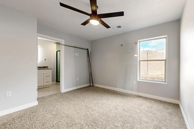 unfurnished bedroom featuring ceiling fan, light colored carpet, and ensuite bathroom