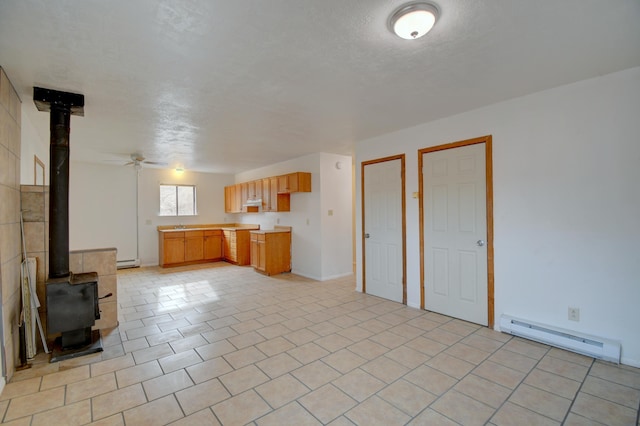 unfurnished living room featuring a wood stove, ceiling fan, a baseboard heating unit, and light tile patterned flooring