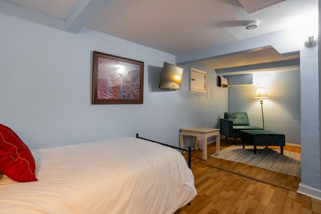 bedroom with beamed ceiling, a wall unit AC, hardwood / wood-style floors, and a textured ceiling