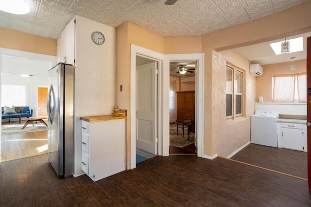 kitchen featuring stainless steel refrigerator, a wall mounted air conditioner, washer / dryer, and white cabinets