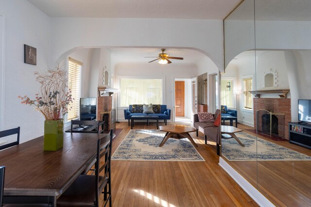 living room featuring a brick fireplace, hardwood / wood-style floors, a healthy amount of sunlight, and ceiling fan