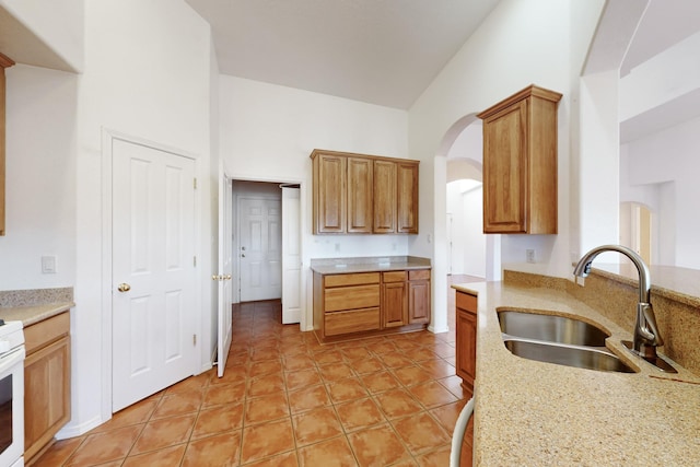 kitchen with a high ceiling, light tile patterned floors, light stone counters, and sink