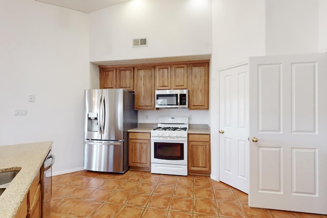 kitchen featuring light stone counters, light tile patterned floors, stainless steel appliances, and a towering ceiling